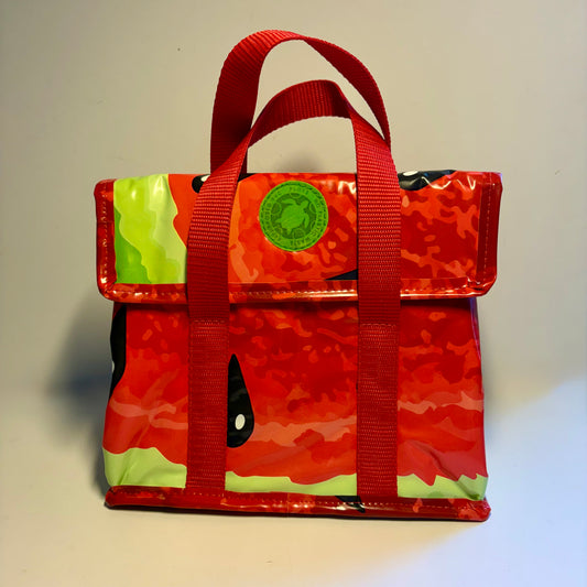 A red watermelon-themed lunch bag with a glossy finish, featuring a red camouflage pattern, light green rind details, and a green circular patch on the front flap.