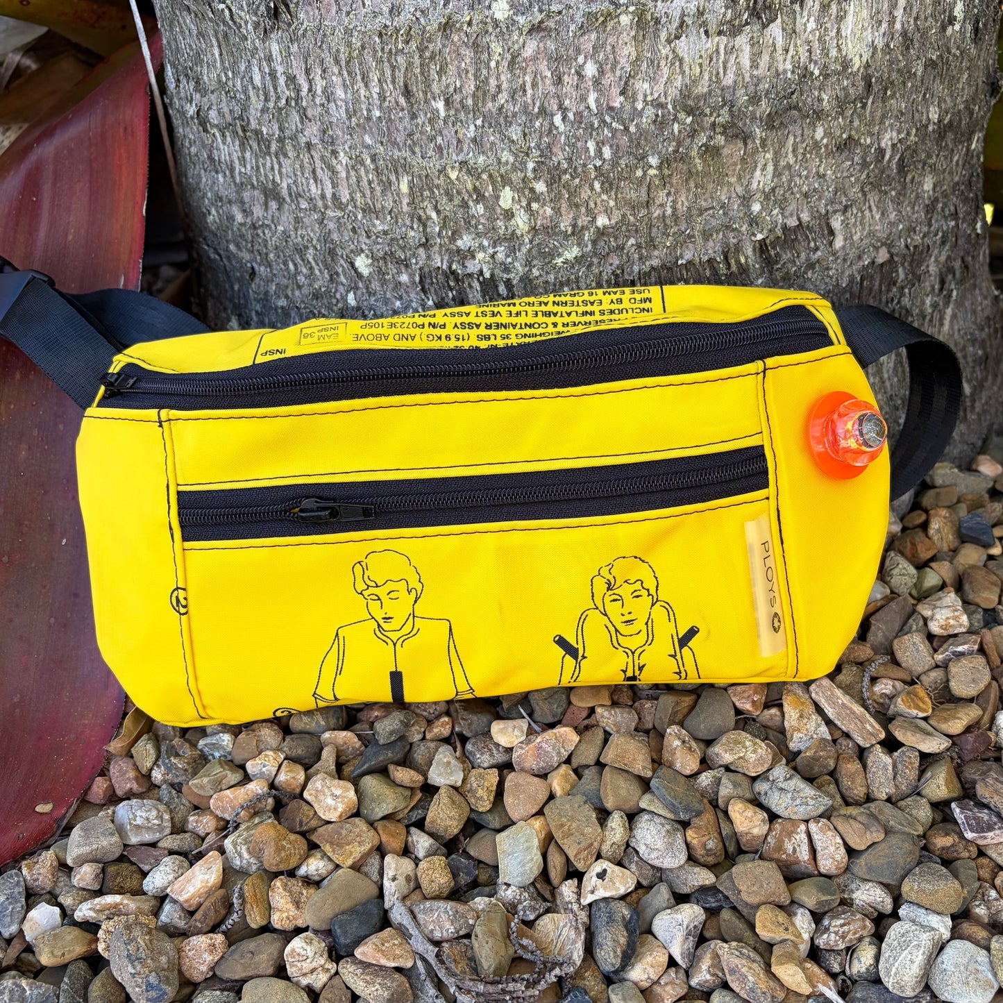 Yellow waist pouch with black zippers and illustrations on a stone surface