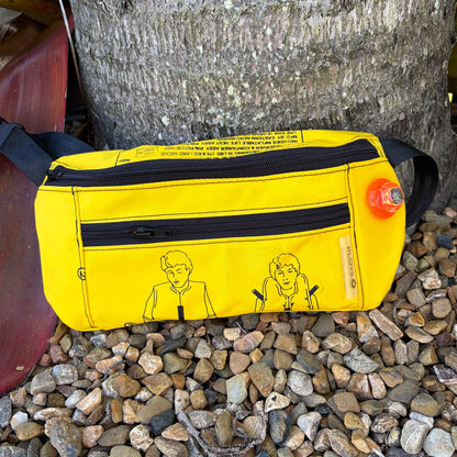 Yellow waist pouch with black zippers and illustrations on a stone surface