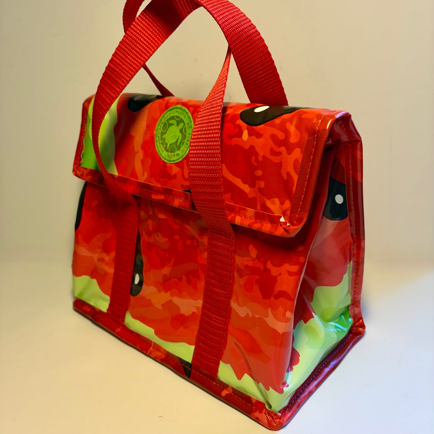 A red and orange camouflage insulated tote bag with green accents, featuring dual top handles, a front pocket, and a circular green brand patch.