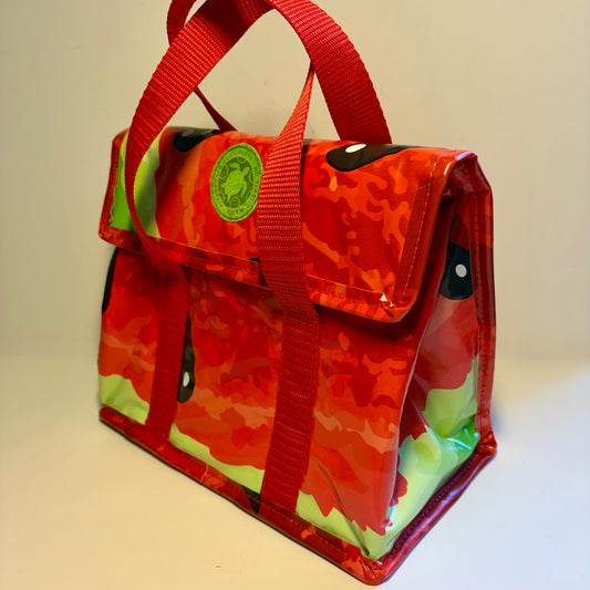 A red and orange camouflage insulated tote bag with green accents, featuring dual top handles, a front pocket, and a circular green brand patch.